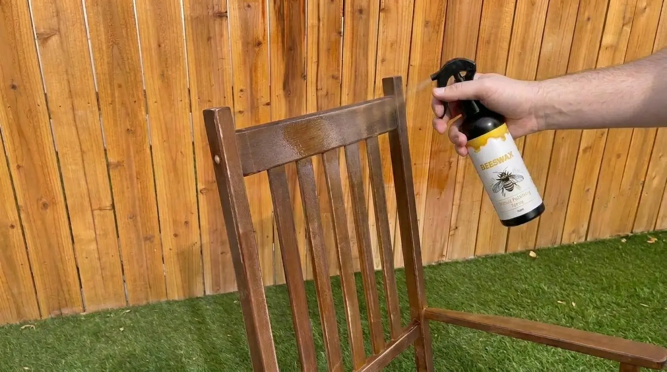 Hand spraying the wood polish product onto an outdoor wood chair in front of a wood fence