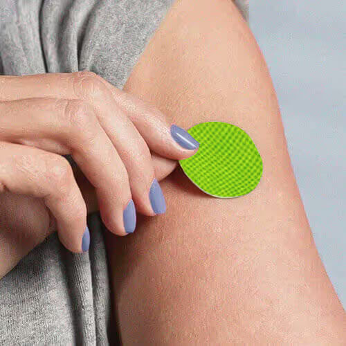 Hand holding a green BugMD Squito Sticker patch up to an arm to show the size of the citronella patch