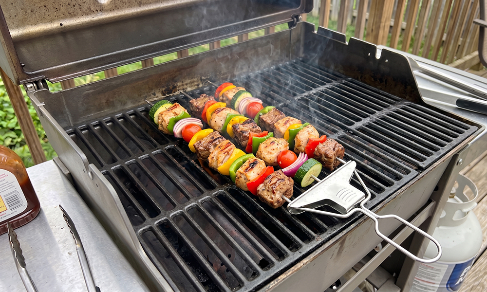 Stainless steel kabob skewers cooking on a charcoal grill alongside shrimp and vegetable skewers