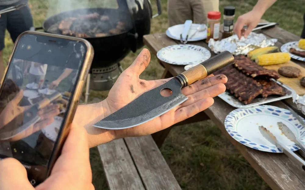 Matsato Osuren knife held at a backyard BBQ next to ribs, corn, and a charcoal grill