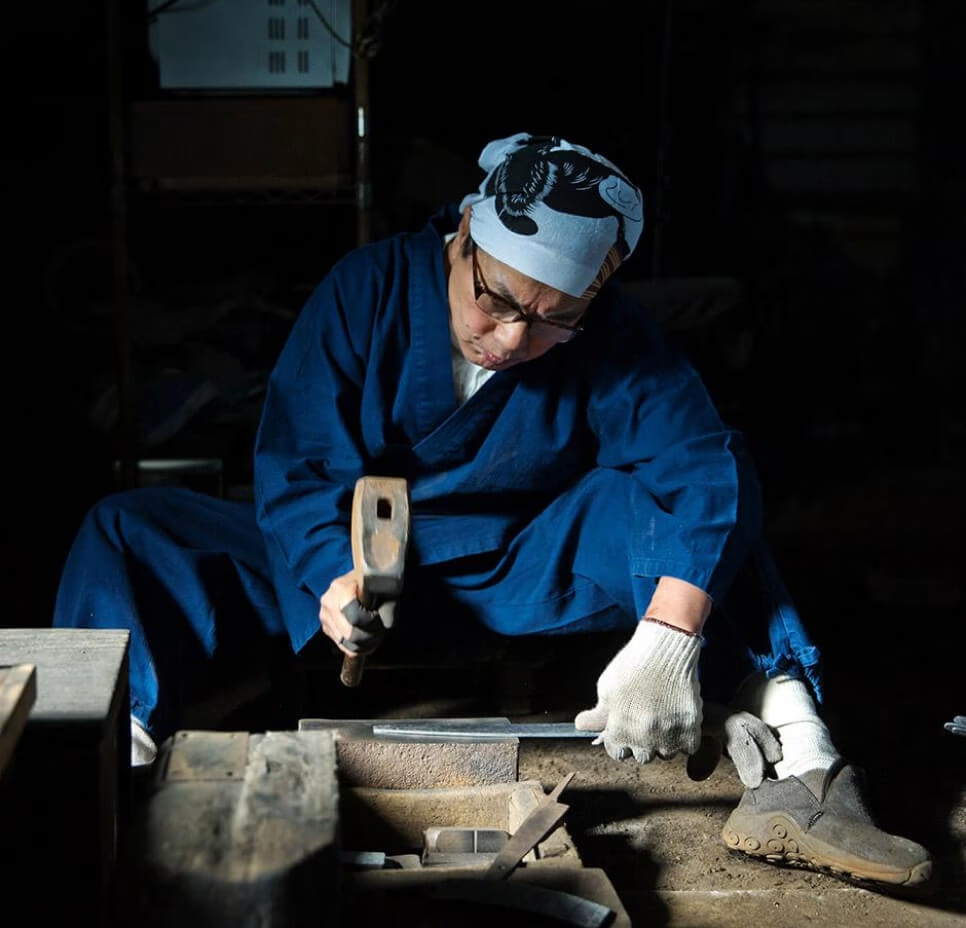 A bladesmith hammering a knife blade by hand in a traditional workshop